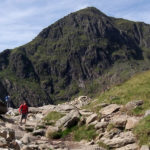 Walker descending the Miners' Track towards Pen y Pass with Yr Wyddfa (Snowdon) rising behind, near Llanberis, Eryri