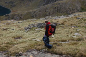 Mark standing on the slopes of Snowdon collecting litter with a grabber and rubbish bag, overlooking a mountain lake during a Snowdonia Society clean‑up.